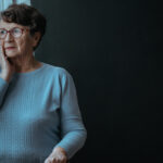 Mujer anciana triste mira por la ventana de su salón.
